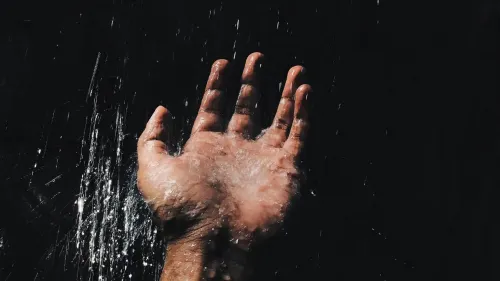 En la foto: Mano de un hombre recibiendo el agua sobre un fondo oscuro.